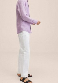 Chemise en lin violet clair, jean en coton blanc, sandales noires. La chemise présente une coupe décontractée et des manches longues, avec une patte de boutonnage.
