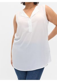 Blusa blanca sin mangas con escote en V y cuello corto, hecha de una tela ligera. Textura suave y dobladillo ligeramente curvado. Combinada con jeans.