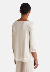 Top beige claro con un corte holgado, mangas tres cuartos y un borde de encaje decorativo en las mangas y el dobladillo. Textura de tejido suave y lisa.
