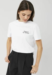 T-shirt en coton blanc à manches courtes, avec l'inscription "Sweet or Sour" brodée en noir sur la poitrine gauche. Assorti à un pantalon noir.