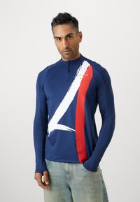 Majica z dolgimi rokavi v mornarsko modri barvi za atletiko s četrtim zadrgo, ki ima bel in rdeč črtast vzorec ter zlati logo "PARIS".