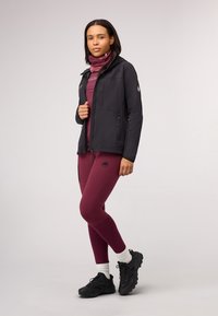 Black softshell jacket with zippered pockets, maroon top, maroon leggings with logo, and black hiking shoes with white socks.