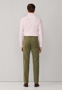 Camisa de manga larga rosa claro, diseñada para un ajuste entallado, combinada con pantalones verde oliva con bolsillos traseros, completado con zapatos marrones.