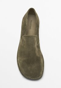 Olijfgroene suède instapschoen met een ronde neus en zonder veters. Het oppervlak is zacht met zichtbare stiksels langs de zool.