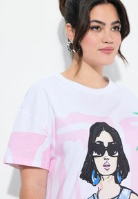 Hvid bomulds t-shirt med en pink og sort illustreret grafik af en kvinde med solbriller, med korte ærmer og rund halsudskæring.