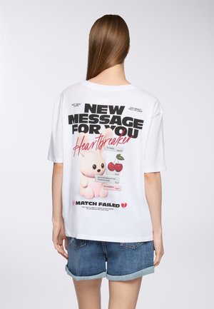 T-shirt bianco oversize con un cartone animato di un coniglio rosa, ciliegie e testo in nero e rosso, con una finitura invecchiata e una vestibilità rilassata.