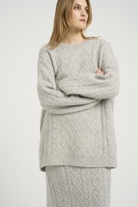 Set de pulover și fustă tricotate de culoare gri deschis, cu un model de tricot în carvăn. Puloverul are un decolteu rotund și un croi oversize. Textură moale și căldură.