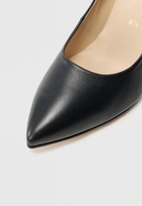 Μαύρο δερμάτινο γυναικείο παπούτσι με ψηλό τακούνι, μυτερή μύτη, λεία υφή και μπεζ εσωτερικό. Μινιμαλιστικός σχεδιασμός χωρίς εμφανείς λεπτομέρειες.