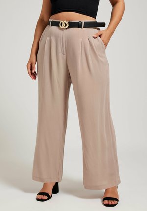 Beige wijde broek met plooien aan de voorkant, voorzien van een zwarte riem met een gouden gesp. Gecombineerd met zwarte sleehakken.