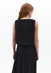 Schwarzes ärmelloses Kleid mit einem strukturierten, wellenförmigen Muster, das an der Taille locker sitzt und eine fließende Silhouette hat.