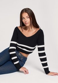 Maglione cropped a righe bianco e nero con scollatura a V, polsini a coste e tessuto morbido, abbinato a jeans a vita alta di colore blu scuro.
