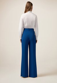 Pantaloni blu a vita alta realizzati in tessuto liscio, caratterizzati da un design sartoriale e gambe larghe, abbinati a una camicia bianca a maniche lunghe.