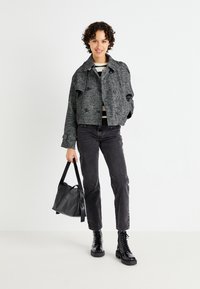 Grå tweed kort jakke med store sorte knapper, stripete topp under, sorte jeans og kraftige sorte snørebåndsstøvler. Svart håndveske.