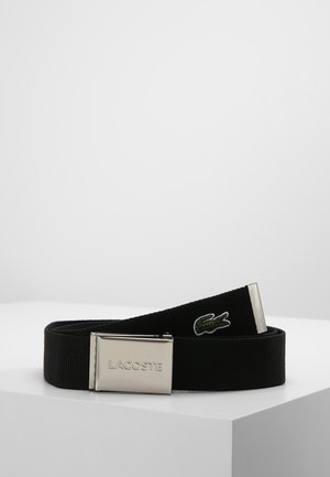 Czarny pas materiałowy z srebrną metalową klamrą wygrawerowaną "LACOSTE" i małym zielonym haftowanym logo krokodyla blisko końca.