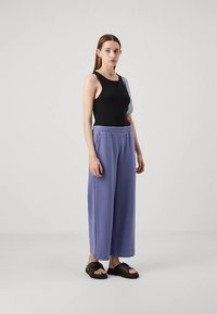 Svart ermeløs topp, løse lavendelfargede bukser med elastisk midje, og svarte slip-in sandaler. Enkel design med avslappet passform.