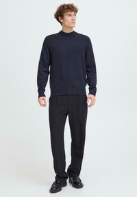 Pulover tricotat bleumarin cu decolteu rotund, manșete și talie cu nervuri, asortat cu pantaloni negri și pantofi negri.