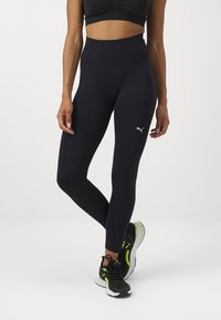 Vysoké, přiléhavé legíny z tmavě modrého materiálu s hladkým povrchem, s malým bílým logem na stehně.