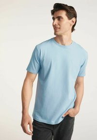 Jasnoniebieska bawełniana koszulka z krótkim rękawem i okrągłym dekoltem, z małym logo na piersi. Noszona z ciemnymi dżinsami.