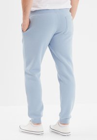 Lichtblauwe sweatpants hebben een taps toelopende pasvorm, een elastische taille, zijzakken en geribbelde boorden. Aan de achterkant bevindt zich een logo-label en een achterzak.