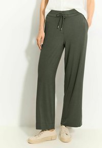 Ciemnozielone spodnie typu wide-leg z miękkiego materiału, z elastycznym paskiem w talii i ściągaczem oraz bocznymi kieszeniami. Prosty, swobodny krój.