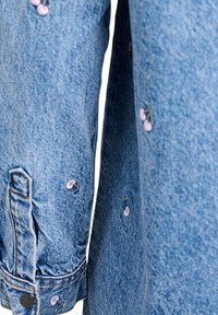 Denim shirt featuring light blue fabric, long sleeves, and pink floral embroidery accents near the cuffs and side.