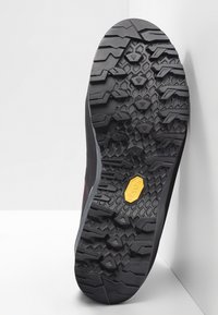 Vandringstekens sula med ett robust svart gummimönster, med djupa spår och en central gul Vibram-logotyp för bättre grepp.