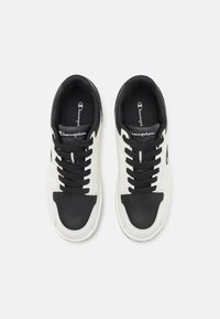Adidași negri și albi cu un superior din piele netedă, șireturi contrastante și o talpă din cauciuc; prezintă branding pe limbă și pe laterale.