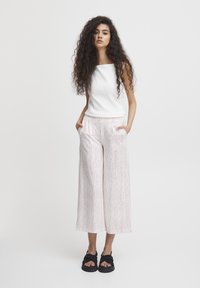 Un haut sans manches blanc associé à un pantalon large à motifs dans des teintes de rose et de blanc, complété par des sandales noires au design noué.