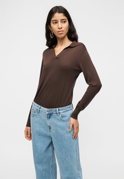 Καφέ μπλούζα πόλο με μακριά μανίκια και V-λαιμόκοψη, συνδυασμένη με ανοιχτό μπλε τζιν φαρδιάς γραμμής. Λείο ύφασμα και εφαρμοστή γραμμή.