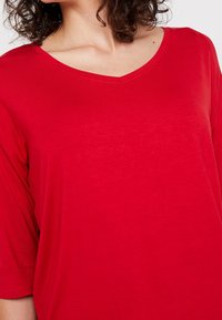 T-shirt rosso a V in morbido e leggero tessuto. Presenta maniche a taglio largo e una superficie liscia con dettagli minimi.
