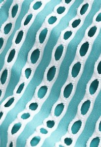 Turkio spalvos audinys su baltomis išsiuvinėtomis ovalo formos išpjovomis, išdėstytomis lygiagrečiais dryžiais, sukuriantis tekstūruotą išvaizdą.