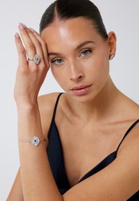 Srebrny zestaw biżuterii składający się z pierścionka, bransoletki i kolczyków z kwiatowym wzorem, zdobiony niebieskimi kamieniami i przejrzystymi dodatkami. Gładka tekstura.