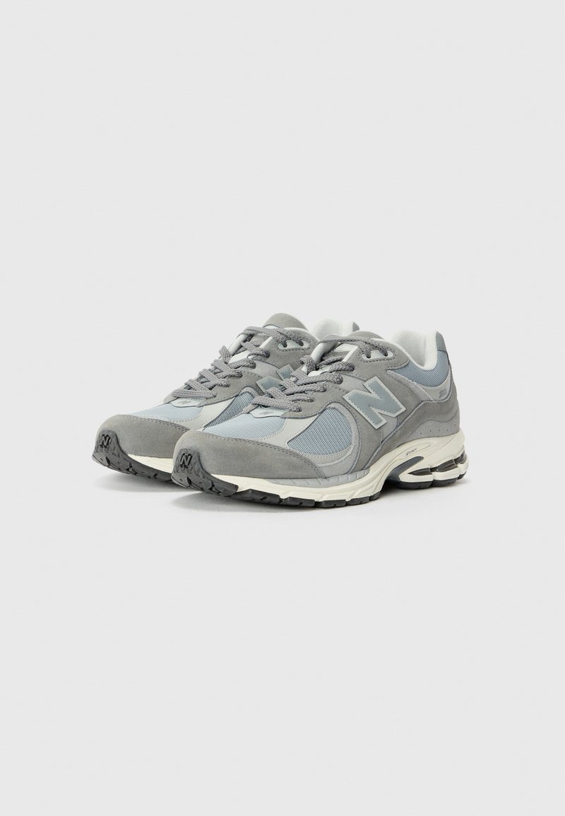 Zapatillas deportivas grises con una mezcla de materiales de ante y malla, que presentan un diseño de cordones, suelas acolchadas y suelas de goma texturizadas.