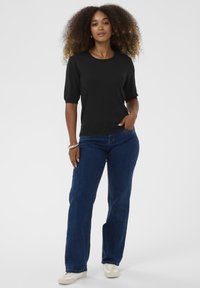 Fekete, rövid ujjú felső, kerek nyakkal, sötétkék farmernadrággal és világos sportcipővel viselve, sima textúrával és laza szabással.