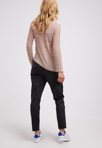 Leichter, strukturierter Pullover in Beige mit einem runden Saum, kombiniert mit schwarzen, schmal zulaufenden Hosen und weißen Sneakern mit blauen Akzenten.