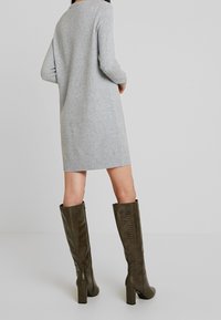 Grå stickad klänning med långa ärmar, i medellång längd till mitten av låren. Kombinerad med höga stövlar i mörk olivgrön med texturerad yta och klackar i blockformat.