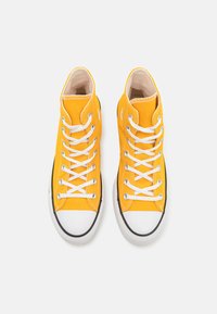 Zapatillas altas de lona amarilla brillante con cordones blancos, acentos negros, puntera redonda y suela de goma texturizada.