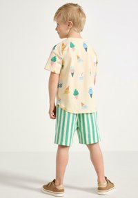 Ljusbeige t-shirt med färgglada glasstryck, kombinerad med randiga shorts i grönt och vitt. Enkel design, bomullsmaterial, avslappnad passform.