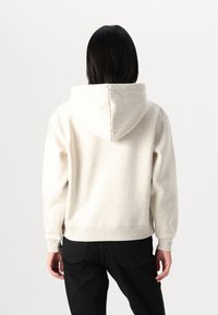 Sweat-shirt à capuche beige clair avec une texture douce, des poignets côtelés et un design court ; porté avec un pantalon noir. Un style simple et fonctionnel.