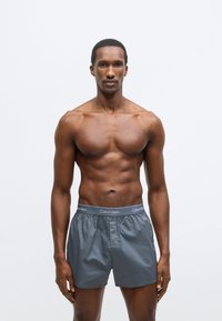 Γκρι μποξεράκια Calvin Klein με ελαστική μέση που φέρει το όνομα της μάρκας. Ελαφρύ ύφασμα, άνετη εφαρμογή, λεία υφή.