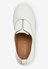 Chaussure slip-on en cuir blanc avec un bout arrondi, présentant un design plissé à l'avant et un doublage intérieur marron avec des détails de marque.