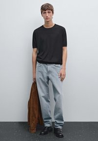 Černé tričko s krátkým rukávem, světle modré rovné džíny, tmavě hnědá semišová bunda přehozená přes levé rameno, černé kožené boty.