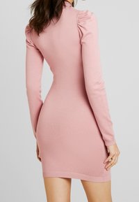 Robe à manches longues et longueur genou en tissu tricoté rose doux. Caractérisée par un détail d'épaule bouffante et des poignets côtelés. Texture lisse avec une silhouette ajustée.