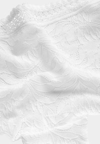 Vitt spets tyg med ett bladmönster och en texturerad bakgrund. Kanterna har en delikat, scalloped finish. Mjukt och lätt material.
