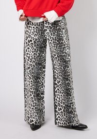 Mustavalkoiset leopardikuvioiset housut paljettikoristeilla, leveälahkeinen malli, teksturoitu kangas, yhdistetty punaisen collegepuseron ja mustien kenkien kanssa.