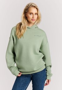Groene hoodie gemaakt van zacht materiaal, met een relaxte pasvorm en geribbelde manchetten. Heeft een klein geborduurd logo op de borst.