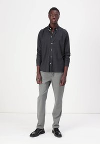 Donkergrijze overhemdd met lange mouwen, gecombineerd met lichtgrijze broek en zwarte schoenen. Het overhemd heeft een klassieke kraag en witte knopen.
