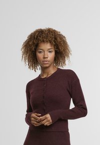 Cardigan en maille bordeaux avec un col rond, des manches longues et des boutons noirs sur le devant. Texture douce, design ajusté à la taille.