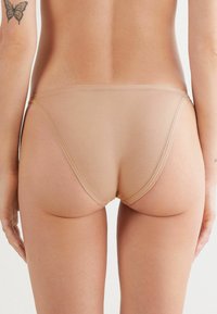 Beige naadloze bikini slipjes met een lage taille, een gladde textuur en minimalistische achterkant, geschikt voor dagelijks gebruik.