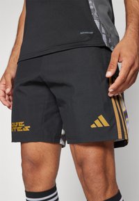 Schwarze Sportshorts mit glatter Textur, ausgestattet mit goldenen Akzenten, drei Streifen und einem Logo; entworfen für Komfort und Leistung.